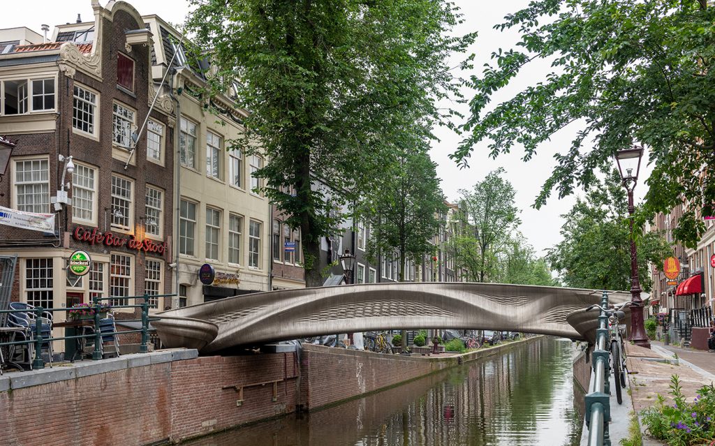 Fig. 6 The MX3D Bridge in its final form, installed and in public use as bicycle- and foot-bridge over the Oudezijds Achterburgwal canal. In a subsequent project, MX3D Smart Bridge, a sensor network was developed and installed in the bridge by The Alan Turing Institute to collect structural measurements such as strain, displacement and vibration, and environmental factors such as air quality and temperature, enabling engineers to measure the bridge's 'health' in real time and monitor how it changes over its lifespan. This data will also enable the bridge to 'understand' what is happening on it, how many people are crossing it, and at what speed (Courtesy MX3D)