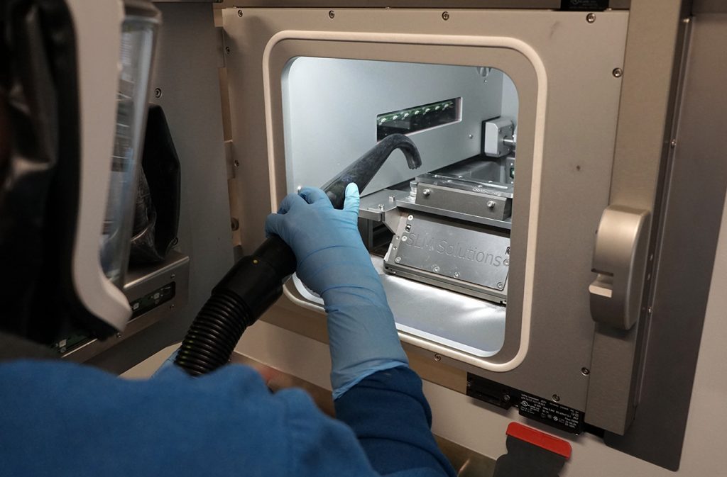 Fig. 4 NanoAL operator cleaning the SLM 125 build chamber after a successful build. The build volume measures 125 x 125 x 125 mm, effectively producing a part with a maximum dimension of 10.2 cm