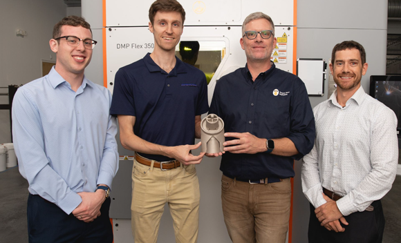 From left, Zachary Iwuc (General Dynamics Electric Boat), Daniel Malta (AMMCON), Joshua Bruns (HII’s Newport News Shipbuilding), and Justin Rettaliata (NAVSEA), pose with the 3D-printed copper-nickel deck drain assembly that will be installed on a Virginia-class submarine. (Courtesy Ashley Cowan/HII)