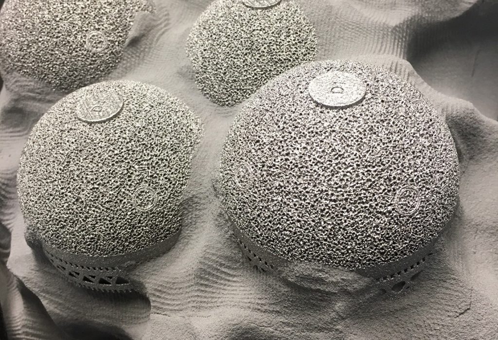 Fig. 2 Additively manufactured (PBF-EB) hip implants from implantcast GmbH shown in a powder 'cake' after the PBF-EB build process. The non-molten powder is blasted off in a Powder Recovery Station and fed back into the process through a special process (Courtesy implantcast GmbH)
