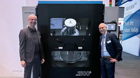 Martin Bullemer, Managing Director AMCM and Andreas Hartmann, CEO/CTO of Solukon in front of the SFM-AT1500-S at Formnext 2024 (Courtesy Solukon)