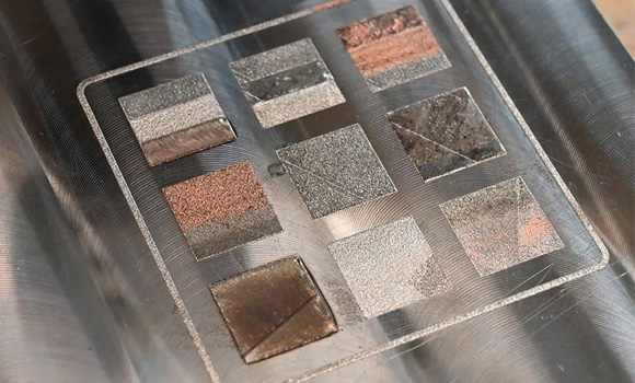 A close-up view of a build plate of test squares featuring the first sintered layer of three metals: stainless steel, Inconel and pure copper. The test squares demonstrated multi-material metal Additive Manufacturing using CIMP-3D's new selective powder deposition system (Courtesy SHAPE Lab, CIMP-3D and 3D Systems)