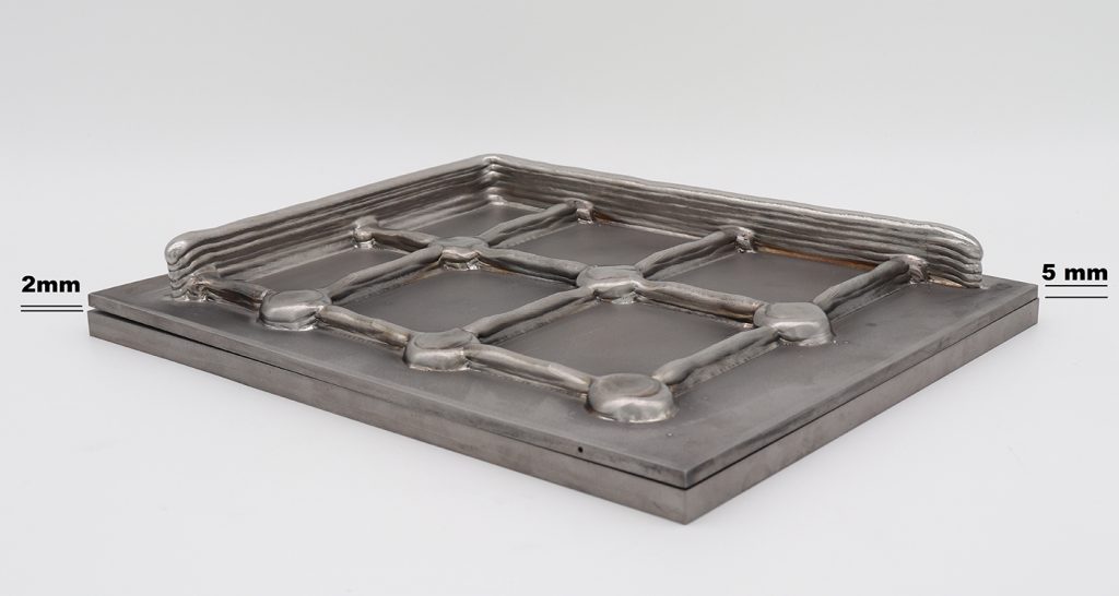 Fig. 7 DED-EB/W structural component (Ti6Al4V) for an application in the aerospace sector built on a 300 x 250 x 5 mm base plate, with a distortion of less than 2 mm. For comparison and highlighting the distortion, a 10 mm base plate is placed beneath (Courtesy Pro-beam Additive GmbH)