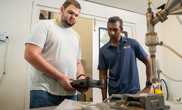 NCAME Research Engineer Mikyle Paul (right) and Hunter Ryan with the centre's VRC Gen IV Cold Spray AM machine (Courtesy NCAME)