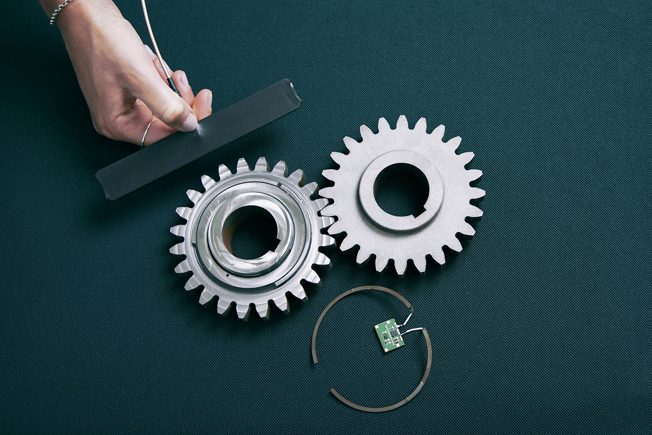 Fig. 1 Sensor-integrated smart gear produced by Fraunhofer IGCV allowing for superior condition monitoring (left), conventional gear (right), additively manufactured antenna and sensor that has been implemented inside the smart gear (bottom), and reading unit for the RFID-based sensor (top)