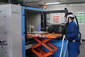 Landon Muhlenkamp, CDME undergraduate student, loading the depowdering machine (Courtesy CDME)