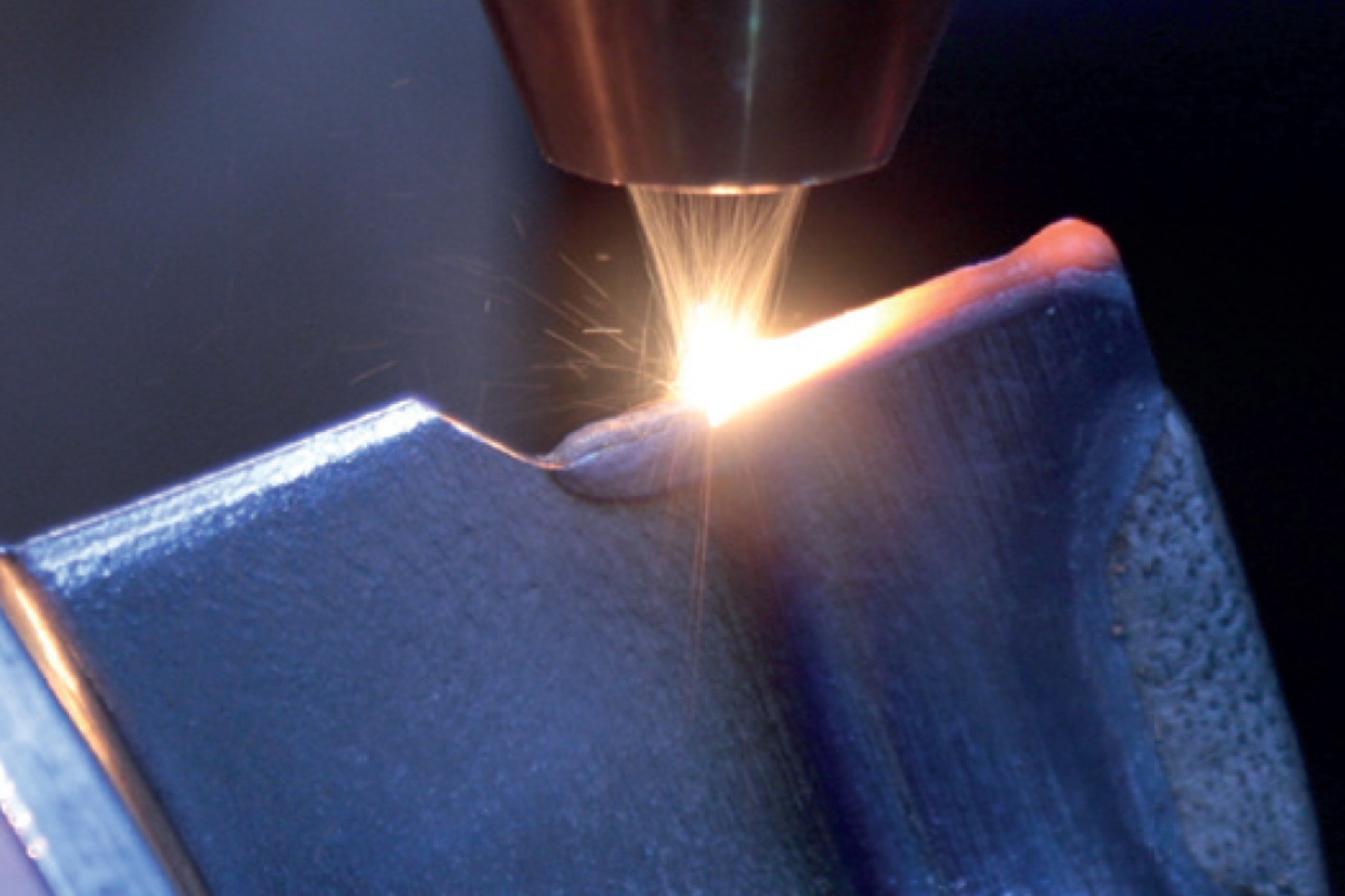 Fig. 1 Laser powder DED repair in operation: powder stream and laser melt pool rebuilding material on a component edge (Courtesy Etxetar)