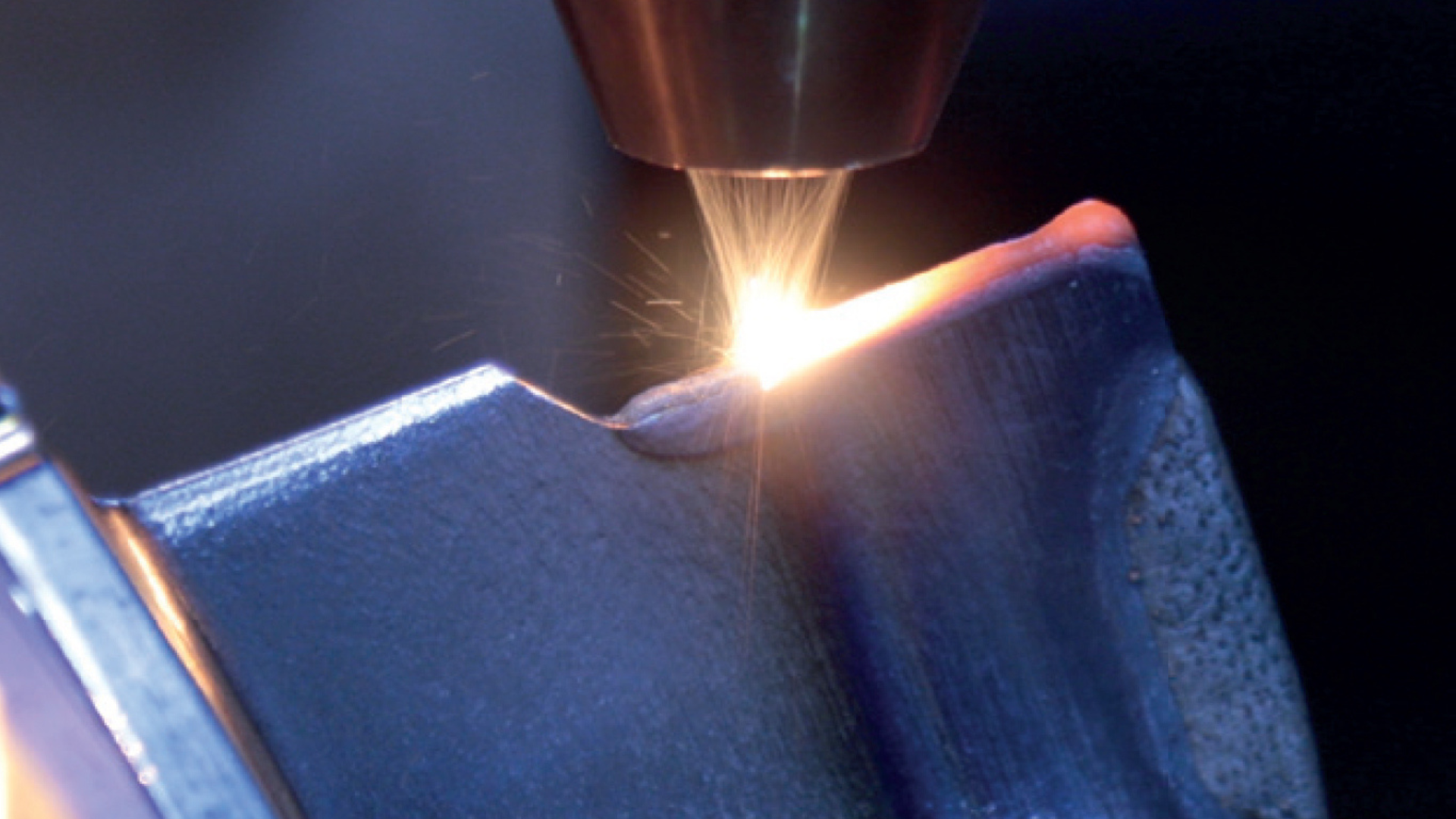Fig. 1 Laser powder DED repair in operation: powder stream and laser melt pool rebuilding material on a component edge (Courtesy Etxetar)
